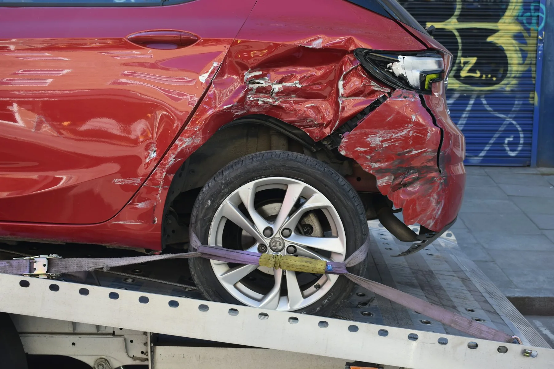 Red hatchback with rear damage on a recovery truck