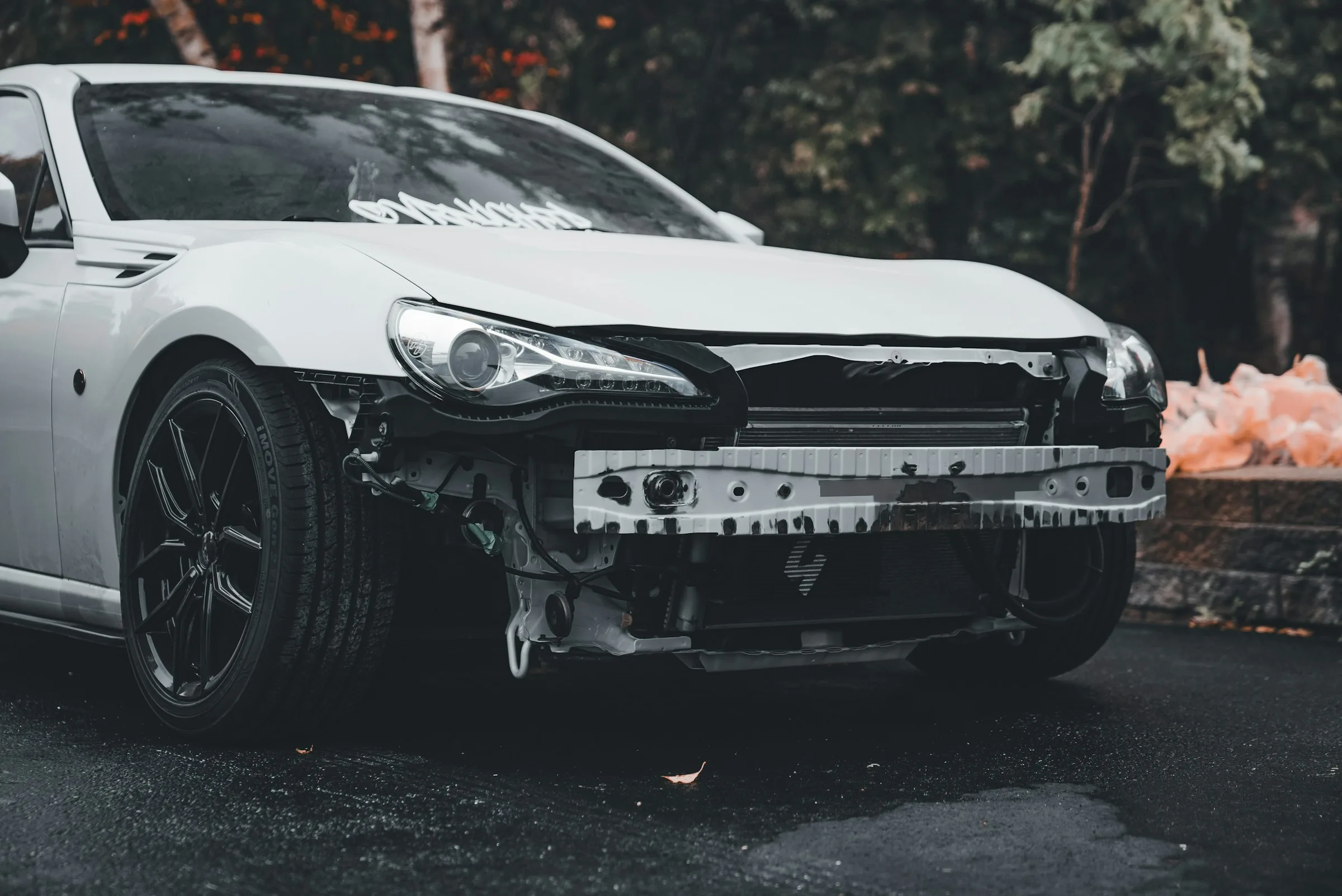 White coupe with the front bumper missing, crash bar and radiator exposed